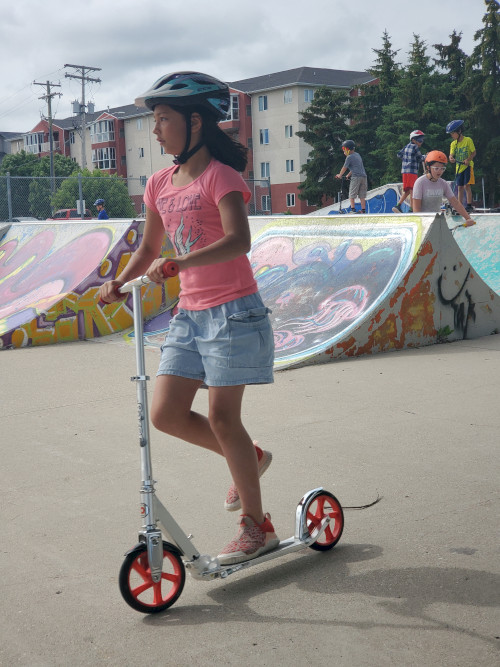 Camper riding a scooter through the skate park.