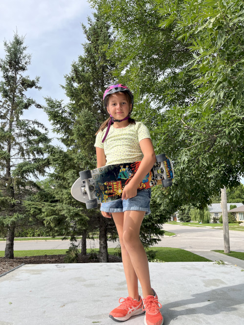 Girl standing in skate park holding a skateboard.