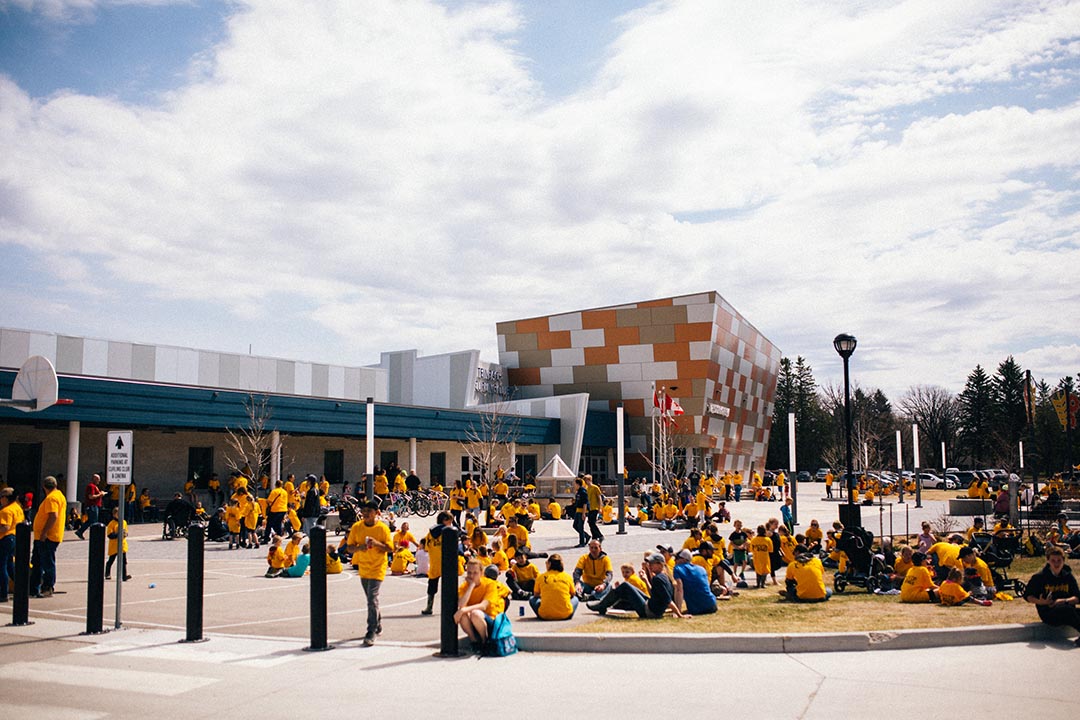 Crowd of Pick Up 'n' Walk volunteers, all wearing yellow shirts, in Steinbach's Community Plaza, outside the T.G. Smith Arena.