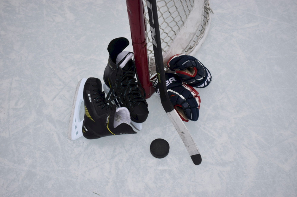 Hockey skates, gloves, a puck and a stick by a goal post.